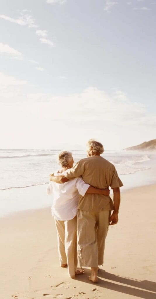 Retirement in Spain An elderly couple walking on the beach arm in arm.